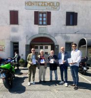 La foto rappresenta i promotori dell'iniziativa con il volantino di sensibilizzazione in mano. A lato una moto verse, sullo sfondo un edificio con la scritta MOntezemolo Foto di gruppo